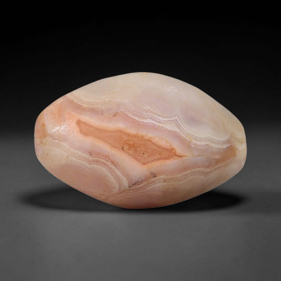 Ancient Pink Banded Agate Bead - Silk Road Indus Valley Barrel Bead, 81BC: Carved from banded agate, the bead is fashioned in a compact barrel form, with a central drilled perforation for suspension. The stone exhibits striking natural banding in soft blush pink, warm peach,