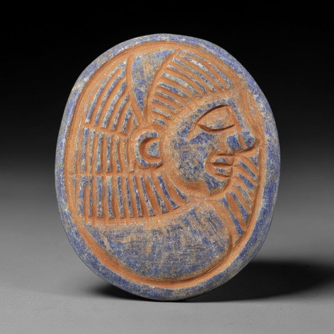 Near Eastern Lapis Lazuli Plaque - Tribal Art Relief, 88BF: Carved from lapis lazuli, the plaque presents a relief profile of a human head, executed in a stylized tribal idiom. The figure is rendered with incised linear detailing to define the headdress, facia