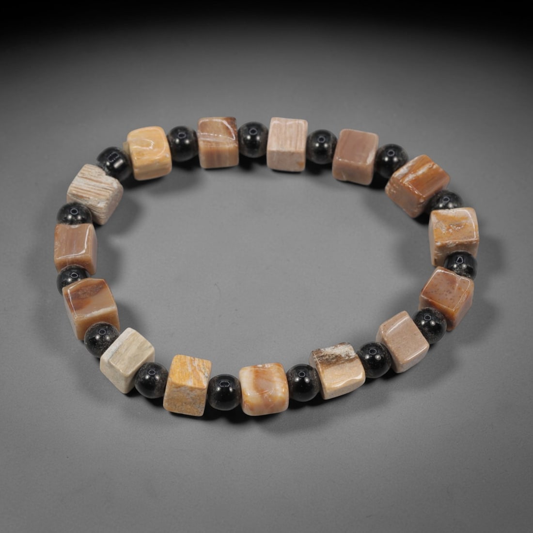 A Chinese Fossilised Wood Bead Bracelet, 20th Century, 86FS: Composed of cushion-shaped beads of fossilised wood with natural banding and minor internal inclusions, the bracelet is strung in a continuous loop. The beads exhibit a smooth, polished surface with s