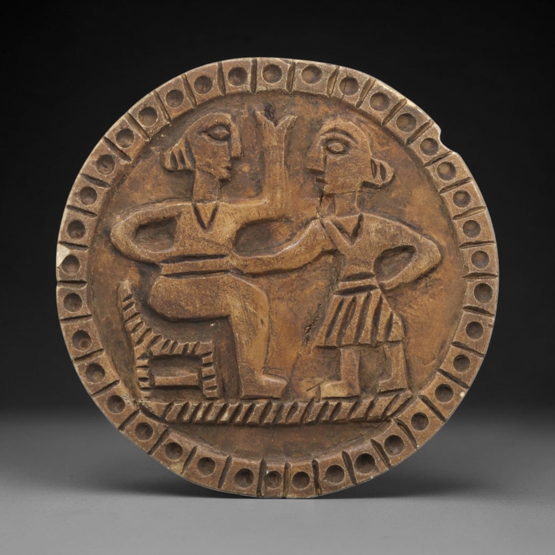 Ancient Steatite Plaque - Near Eastern Dual Figure Relief, 31ZY: Carved from steatite, this circular plaque features a relief depiction of two anthropomorphic figures engaged in an interaction, rendered in the stylized, schematic artistic tradition of the Ancient N