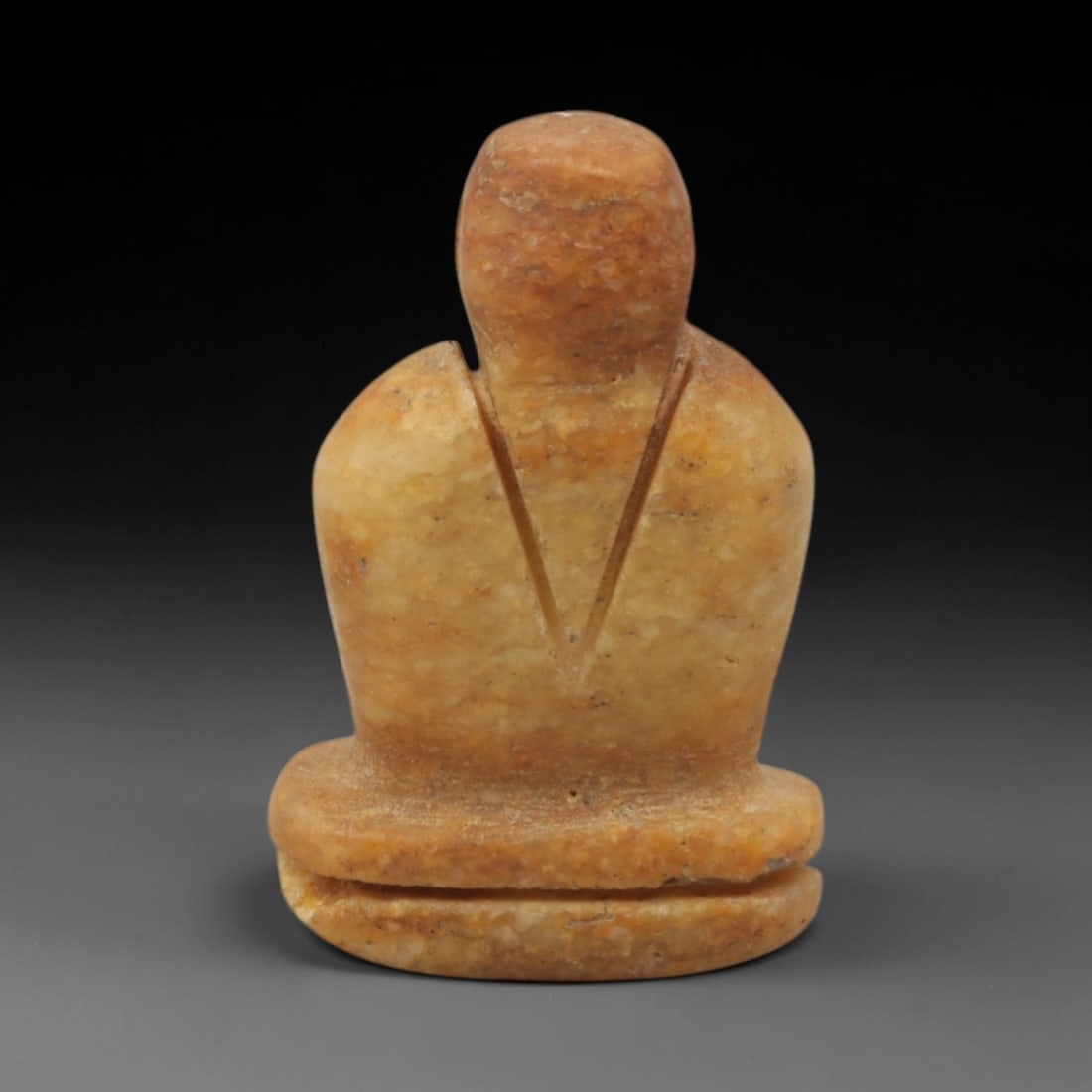 Ancient Stone Bust - Near Eastern Anthropomorphic Figurine, 61XR: Carved from warm orange-brown stone, this miniature anthropomorphic bust features a rounded head, broad shoulders, and a V-shaped incised detail on the chest, seated atop a double-layered base. The si