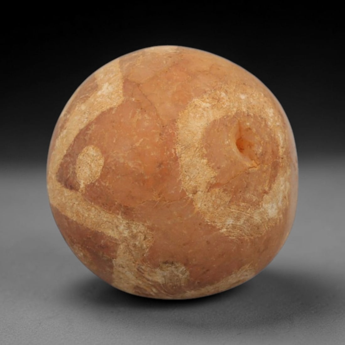 Ancient Carnelian Etched Bead - Gandhara Spherical Bead, 9XY: The bead is carved from carnelian, a semi-precious chalcedony, with a spherical form and a laterally drilled suspension hole. Its surface features an etched white geometric pattern of angular bands an