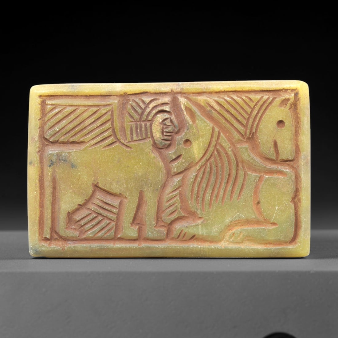 Near Eastern Serpentine Plaque - Tribal Art Figure & Animal Relief, 97ZY: Carved from serpentine, this rectangular plaque features a deeply incised relief depicting a stylized anthropomorphic figure positioned above a stylized large animal form, executed with expressive tri