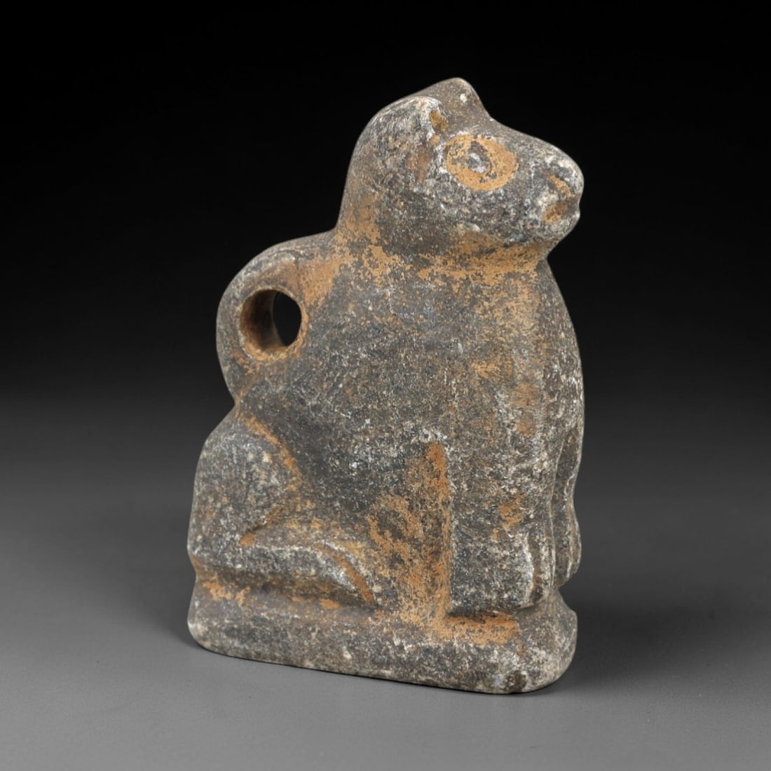 Ancient Stone Zoomorphic Amulet - Near Eastern Animal Figure, 3AM: This amulet is carved from dark speckled stone, depicting a stylized quadrupedal animal in a seated posture, with incised linear detailing defining the facial features, ears, and limbs. The piece refl