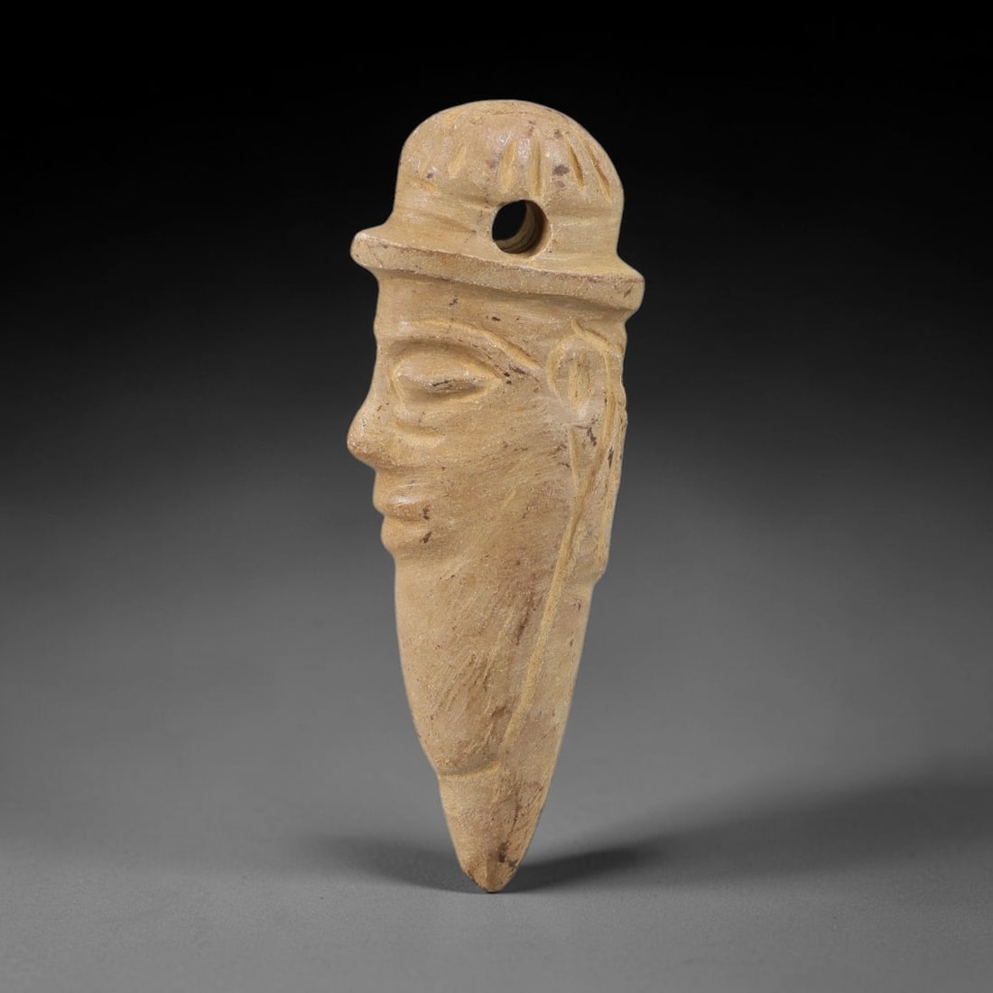Ancient Stone Human Head Amulet - Near Eastern Carved Pendant, 51BA: Carved from light-colored hardstone, this amulet takes the form of a stylized human head in profile, rendered in three dimensions with detailed, naturalistic carving. The figure wears a patterned head