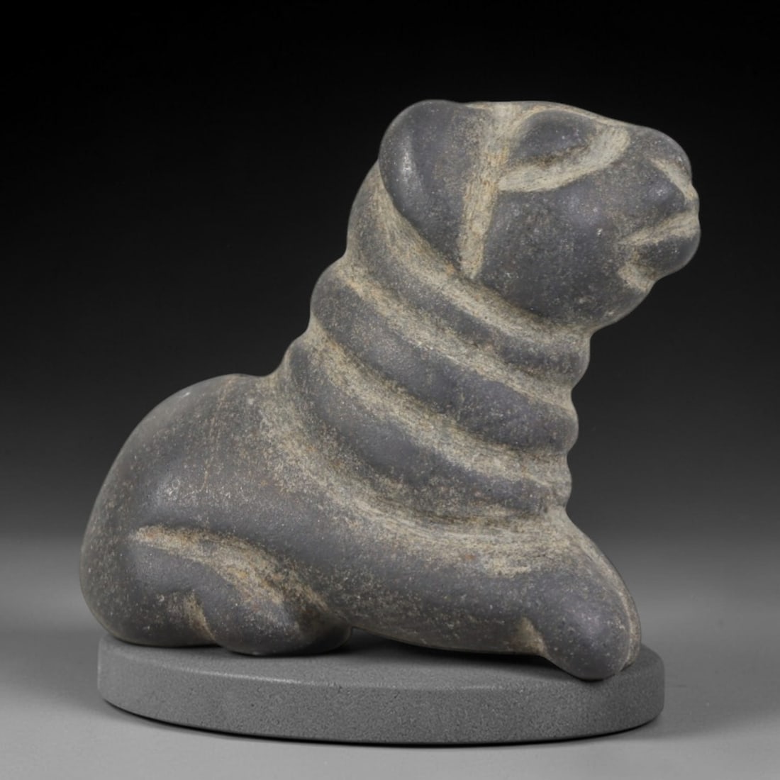 Ancient Stone Recumbent Feline - Egyptian Animal Figurine, 75AP: This artifact is carved from dark gray stone with a weathered, matte patina and subtle mineral inclusions, exhibiting stylized feline features consistent with ancient Egyptian stoneworking techniques.