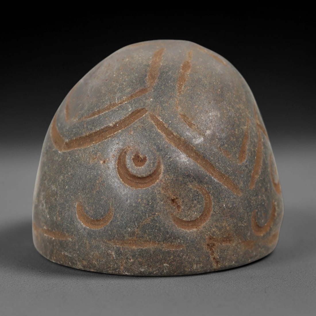 Ancient Stone Weight - Near Eastern Crescent Motif, 59AM: This conical weight is carved from dark stone, featuring incised linear and crescent motifs across its surface, executed in a simple relief style consistent with ancient Near Eastern utilitarian artif
