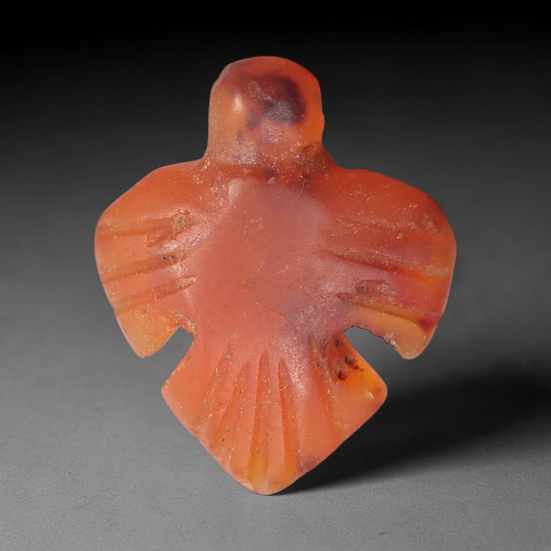 Ancient Agate Bird - Egyptian Amulet Figurine, 38XS: This amulet is carved from warm orange-red agate with natural dark inclusions, exhibiting the characteristic translucency and subtle banding of ancient Egyptian glyptic craft. The form is a stylized a