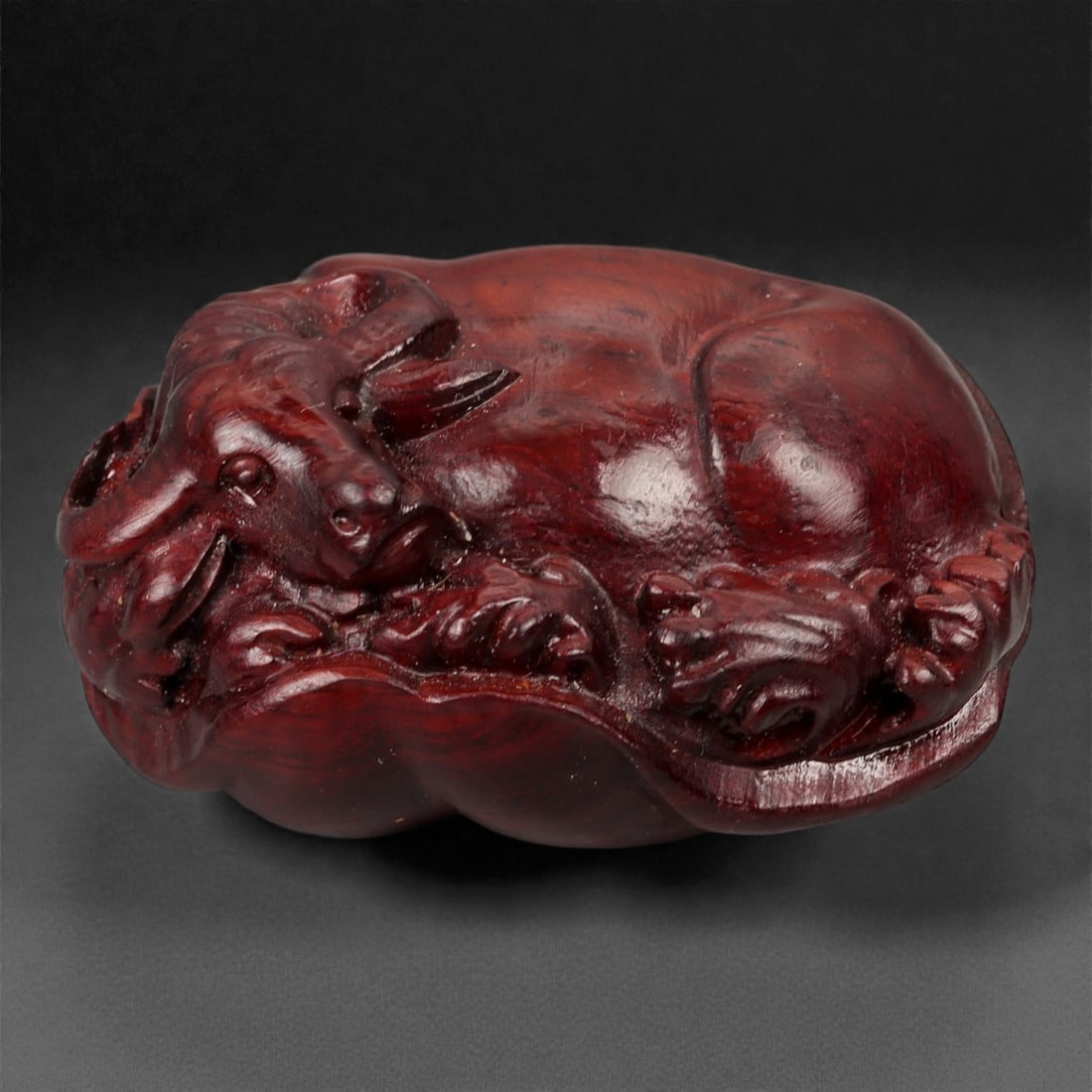 A Chinese Wood Buffalo Carving, 20th Century, 51YB: Carved from dense reddish-brown wood with a smoothly polished surface and visible natural grain, the figure represents a water buffalo shown recumbent with the legs tucked beneath the body and the hea
