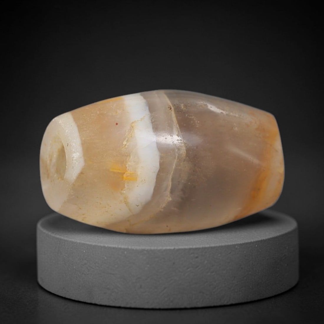 Ancient Agate Bead - Bactrian Amulet, 69BD: This artifact is crafted from banded agate, exhibiting soft translucent bands of pale amber, creamy white, and subtle greyish hues with delicate mineral veining, shaped into a smooth barrel form throu