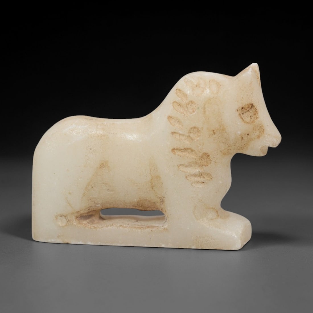 Ancient Marble Horse - Near Eastern Amulet Figurine, 91XR: Crafted from pale marble, this small amulet depicts a stylized recumbent horse. The compact, rounded body rests on a solid base, with a rectangular suspension hole carved beneath the torso, confirming
