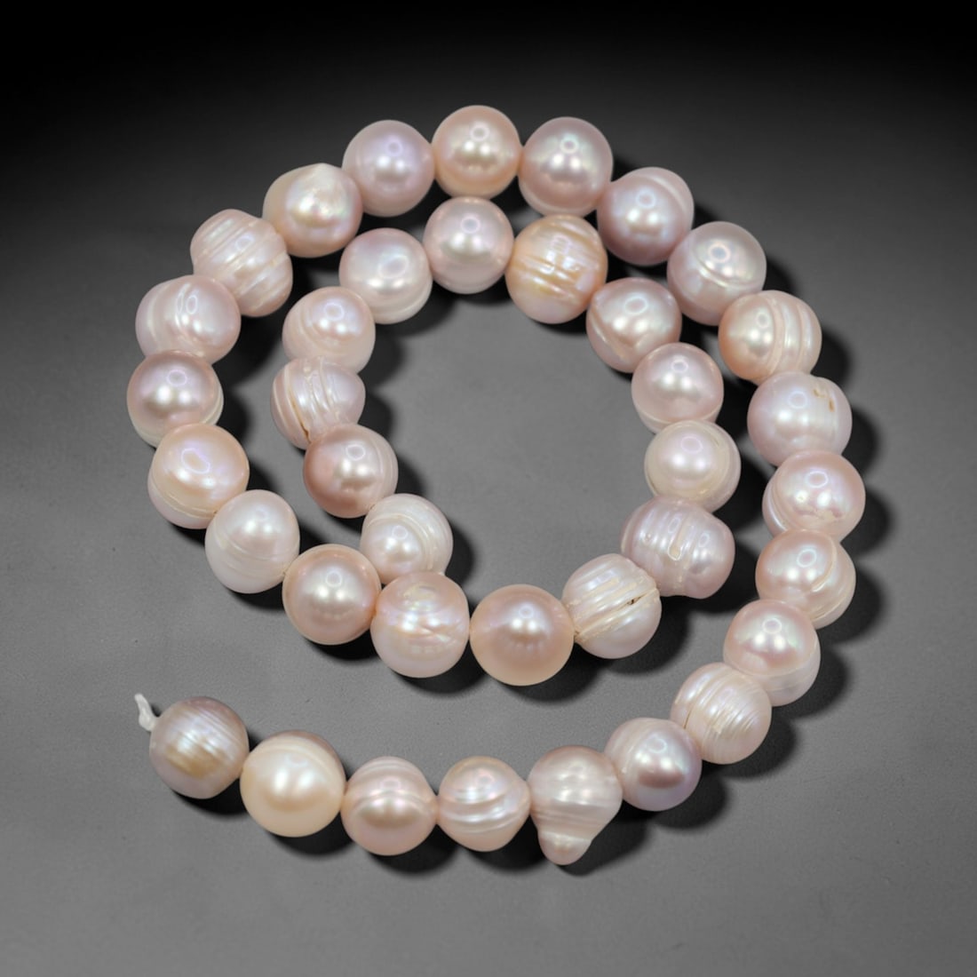 A Strand of Cultured Pearls, 20th Century, 87ZJ: Composed of near-round cultured pearls with a soft peach-pink body color and subtle iridescent overtones, the strand is strung in a single continuous line. Each pearl exhibits a smooth, lustrous surfa