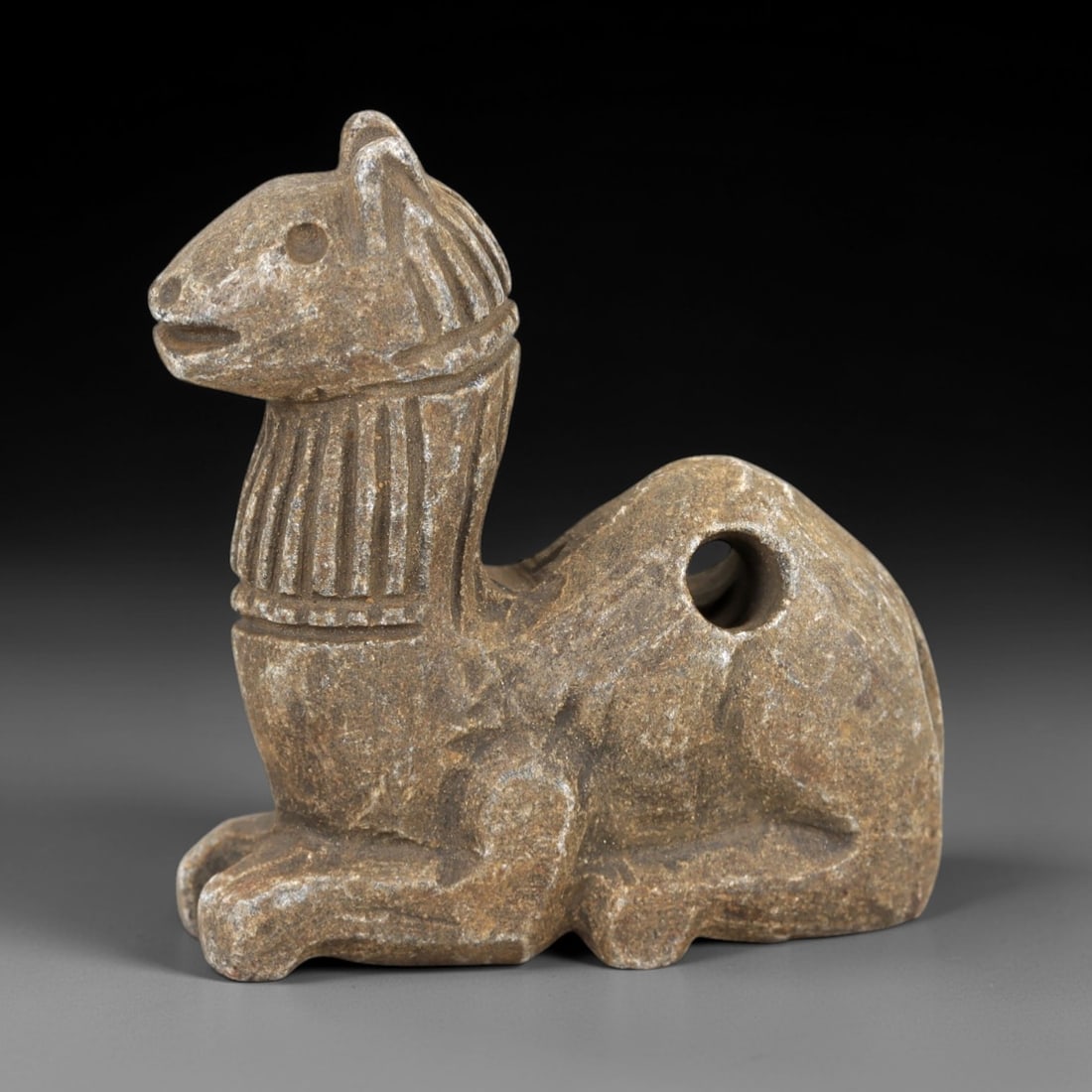 Ancient Stone Camel Amulet - Near Eastern Desert Talisman, 26AM: This amulet is carved from warm beige stone with natural speckling and a weathered patina, depicting a stylized camel in a recumbent, crouched posture. The piece features incised linear detailing defi