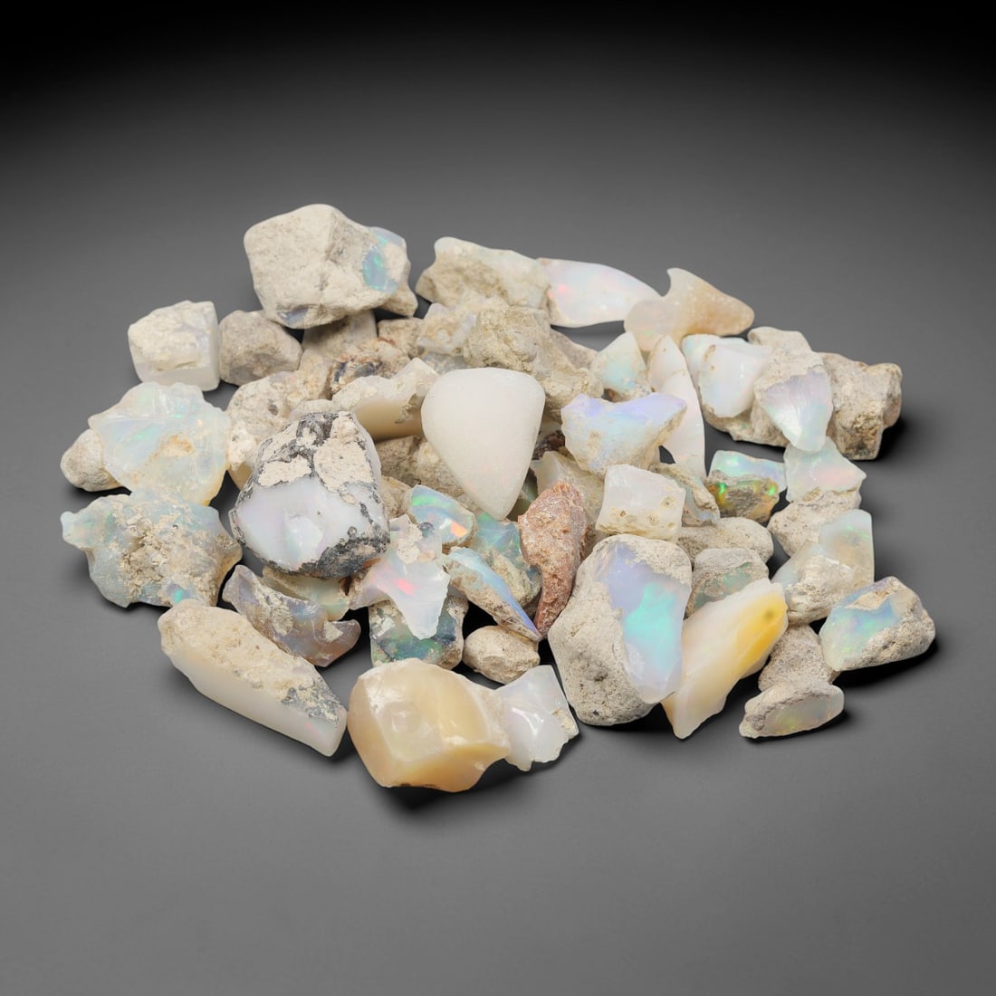 An Ethiopian Welo Opal Rough Lot, 47.23g, 50ZH: A parcel of rough Welo opal, with individual pieces ranging from 1-2 cm in size. The specimens exhibit a milky to translucent base, with visible play-of-color displaying flashes of blue, green, yellow