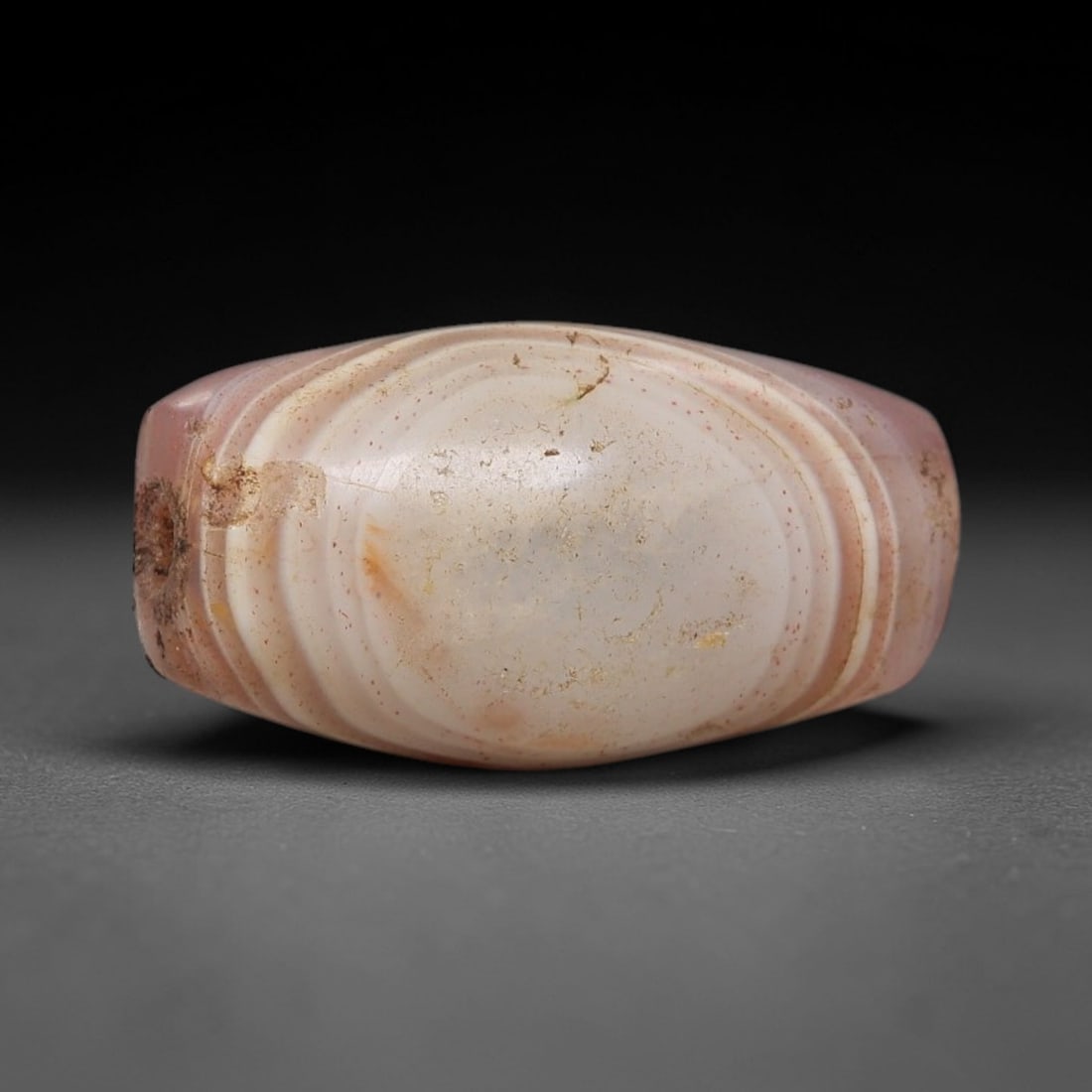 Ancient Agate Bead - Indus Valley Silk Road Barrel Bead, 48BC: Carved from translucent banded agate, the bead is fashioned in a compact barrel form, with a central drilled perforation for suspension. The stone exhibits soft concentric banding in pale pink, milky