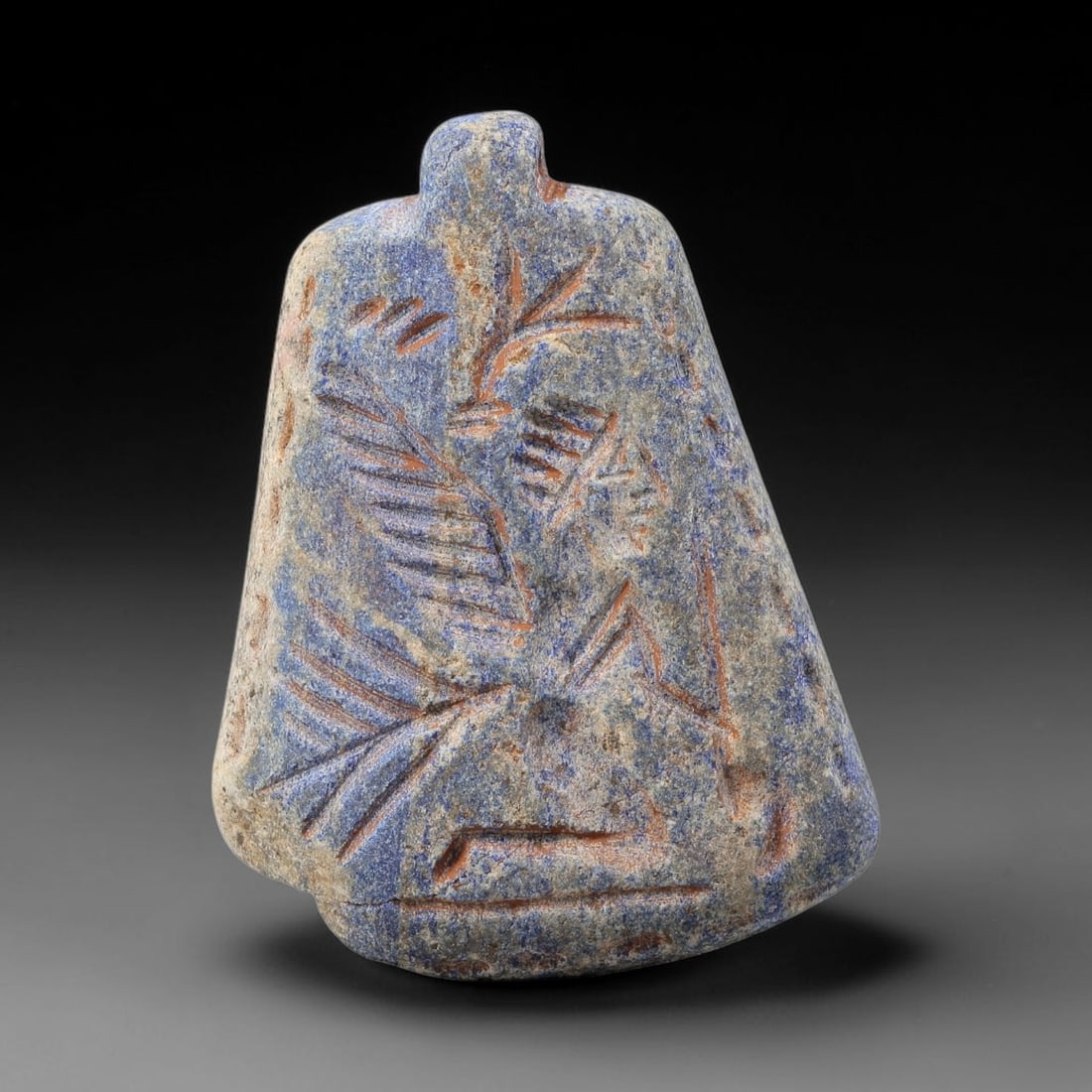 Ancient Lapis Amulet - Near Eastern Winged Figure, 75BF: Carved from lapis lazuli, the amulet is a bell-shaped plaque with a perforated suspension knob at the upper edge, designed for wearable use. The front face is incised with a stylized winged humanoid f