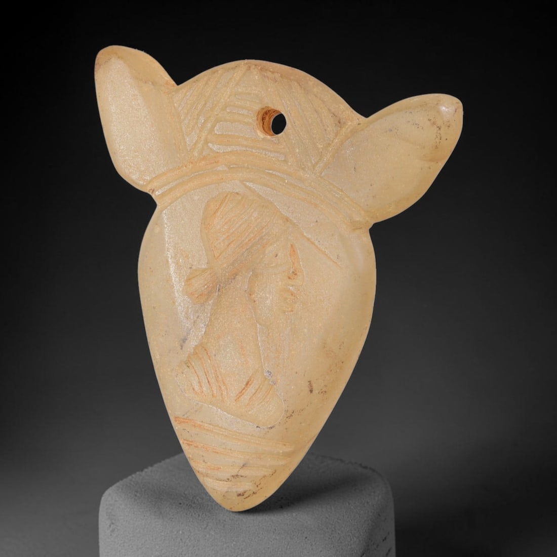 Ancient Chalcedony Head Amulet - Near Eastern Plaque, 23FY: Carved from a pale, translucent chalcedony, this amulet takes the form of a stylized bull's head or shield-shaped plaque, with a small suspension hole drilled at the top center, characteristic of anci