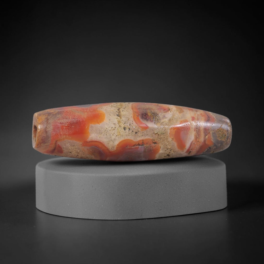 Ancient Agate Bead - Silk Road Bactrian, 4BC: Carved from banded carnelian agate, the bead is fashioned in a bi-conical barrel form with a central perforation for suspension. The stone displays striking natural concentric banding in vibrant orang