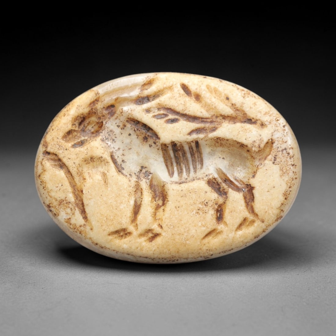 Ancient Agate Intaglio Bead - Near Eastern Ibex Motif, 39ZW: Carved from warm banded agate, this oval intaglio bead features a recessed depiction of a standing ibex with curved horns, accompanied by a stylized vegetal branch, characteristic of ancient Near East