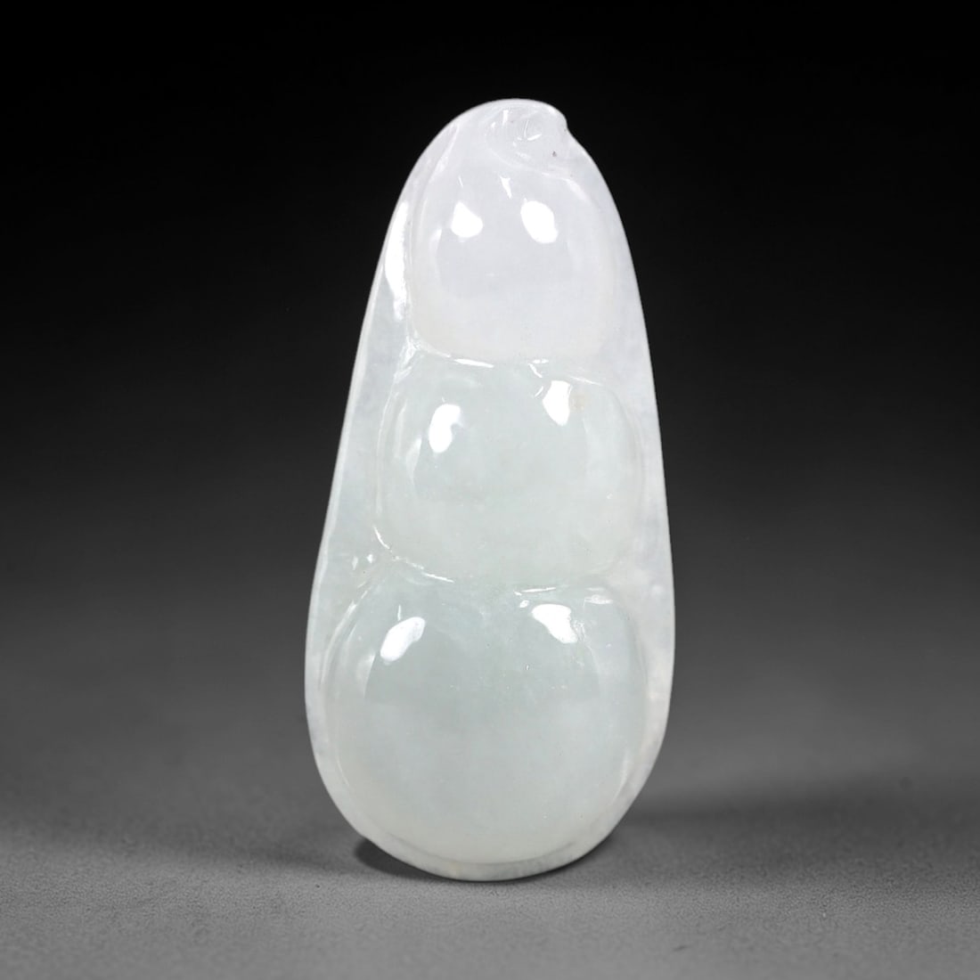 A Chinese Icy Jadeite Jade Bean Pendant, 20th Century, 52AB: Carved from translucent icy jadeite with a pale milky-white to light greenish-white hue and minor natural inclusions, the pendant is shaped as a stylized three-segmented bean pod. Smooth, rounded cont