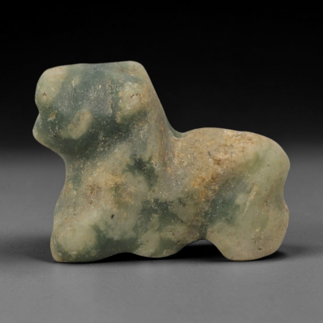 Ancient Stone Zoomorphic Amulet - Near Eastern Pendant, 22XQ: Carved from a mottled pale green and beige stone with natural veining, this amulet depicts a highly stylized zoomorphic form, likely a feline or small ruminant, with a rounded head, compact body, and