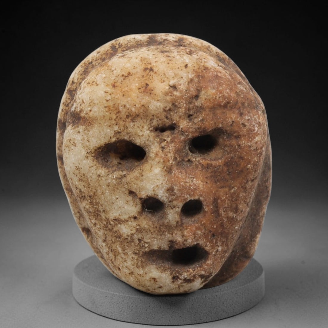 Ancient Stone Maskette - Medieval Human Face Figurine, 31BH: A carved stone maskette of rounded form, fashioned from a single piece of weathered marble with natural tan and brown mineral staining. The front is carved in deep relief to depict a stylized human fa