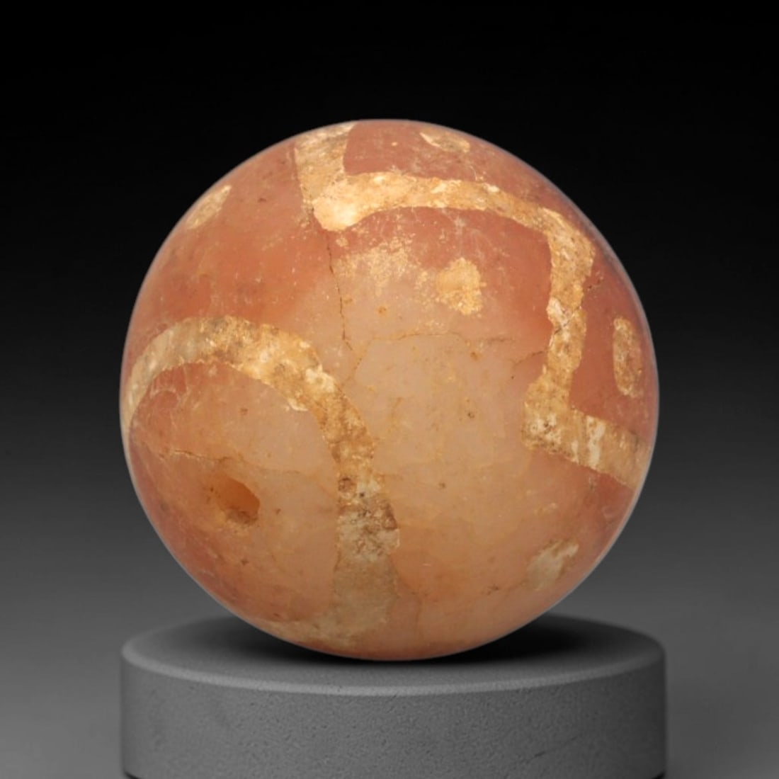 Ancient Carnelian Etched Bead - Gandhara Spherical Bead, 27XY: The bead is fashioned from carnelian, a semi-precious chalcedony, with a spherical form and a laterally drilled suspension hole for wear. Its surface is decorated with an etched white geometric patter