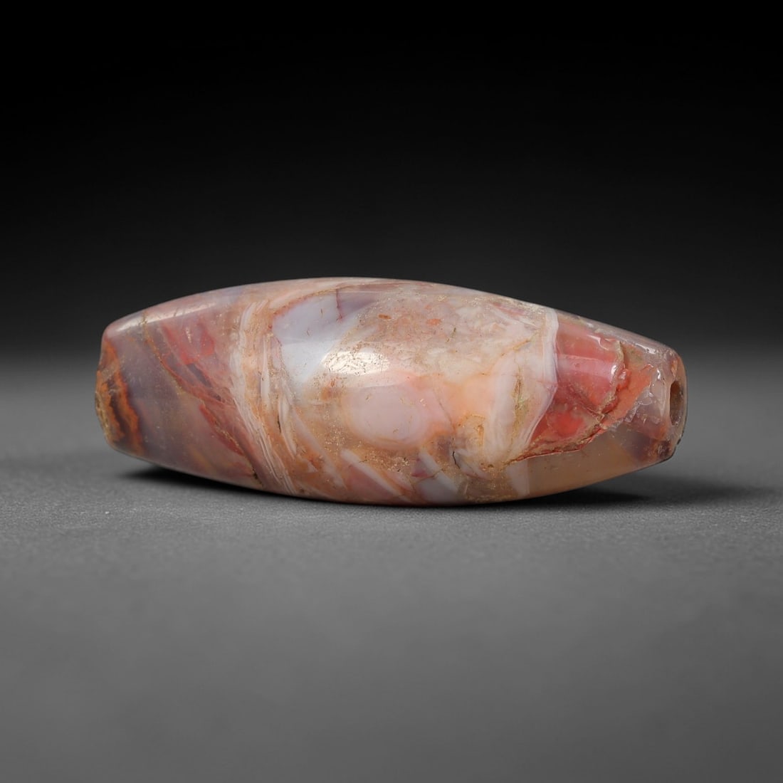Ancient Agate Barrel Bead - Silk Road Indus Valley Bead, 33BC: Carved from multicolored banded agate, the bead is fashioned in an elongated barrel form, with a central drilled perforation for suspension. The stone exhibits striking natural banding in deep red, pa