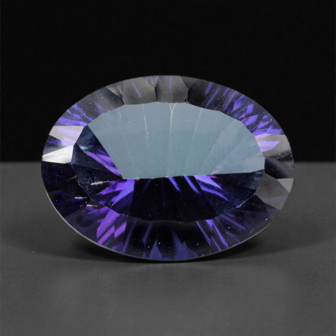 18.80 Carats Deep Violet-Blue Topaz - Natural Brazilian Stone - 19.6 x 14.5 x 9.2 mm, 44XK: A striking display of depth and brilliance, this large oval-cut topaz radiates an intense violet-blue hue that captures attention from every angle. Its expertly faceted crown enhances the gem's natura