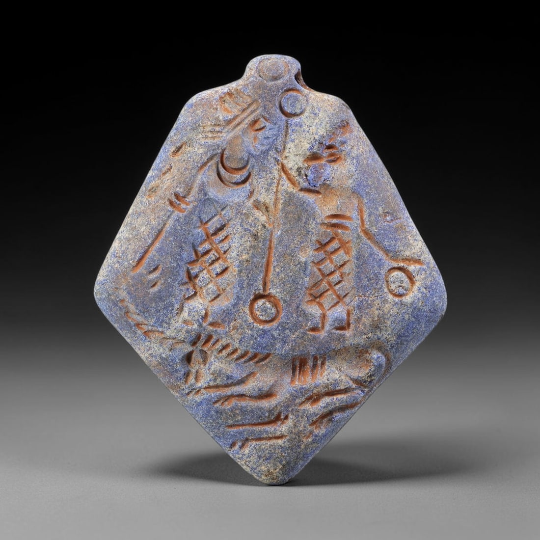 Ancient Lapis Amulet - Near Eastern Figural Scene, 76BF: Carved from lapis lazuli, the amulet is a diamond-shaped plaque with a perforated suspension knob at the upper edge, designed for wearable use. The front face is incised with a detailed figural compos