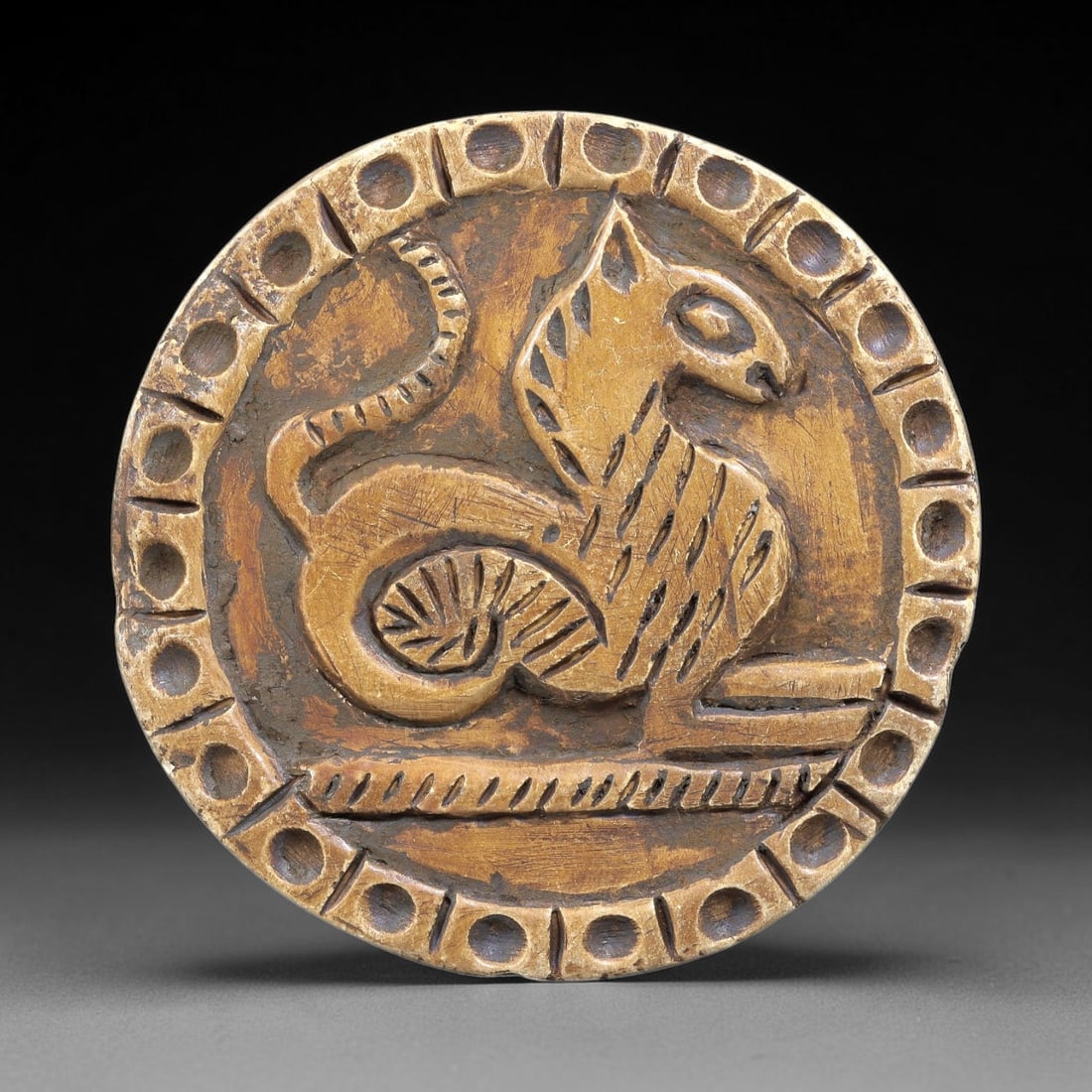 Ancient Steatite Plaque - Near Eastern Seated Feline Relief, 95BE: Carved from steatite, the circular plaque features a raised relief of a seated feline, likely a lion or big cat, rendered with incised linear details defining its body, striped patterning, and curled