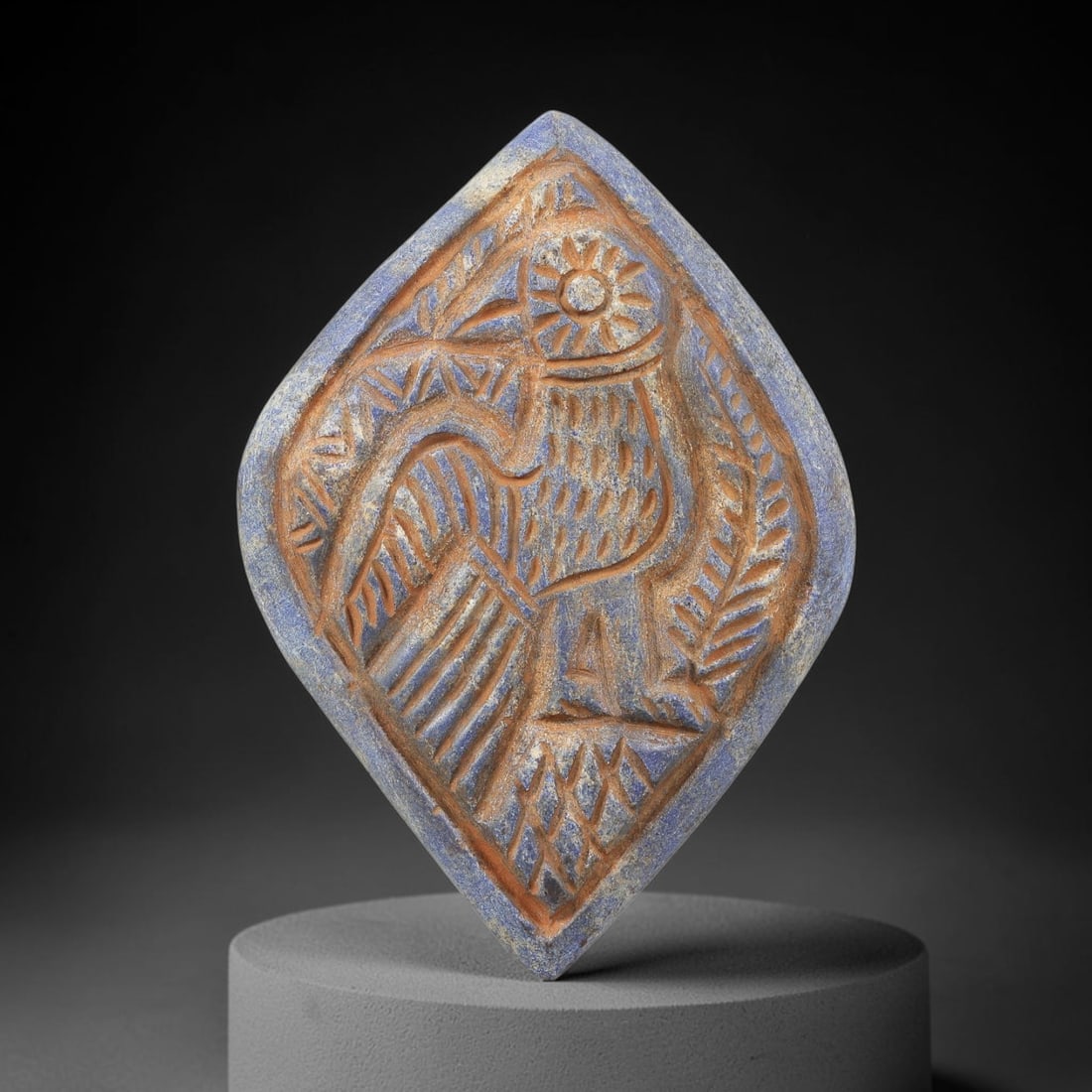Near Eastern Lapis Lazuli Plaque - Tribal Art Bird Relief, 3BG: Carved from lapis lazuli, this diamond-shaped plaque features a relief depiction of a stylized bird with outstretched wings, surrounded by flanking foliate motifs and a central solar symbol above the