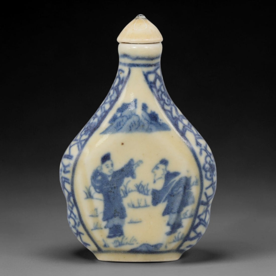 A Chinese Porcelain Snuff Bottle, 20th Century, 51BE: Crafted from porcelain with a pale cream glaze and decorated in underglaze blue, the snuff bottle features a flattened, faceted pear-shaped body, a short cylindrical neck, and a conical stopper. The m