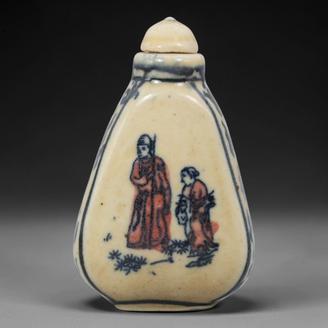 A Chinese Porcelain Snuff Bottle, 20th Century, 55BE: Crafted from porcelain with a pale cream glaze and decorated in underglaze blue with copper red accents, the snuff bottle features a flattened, tapering body, a short cylindrical neck, and a domed sto