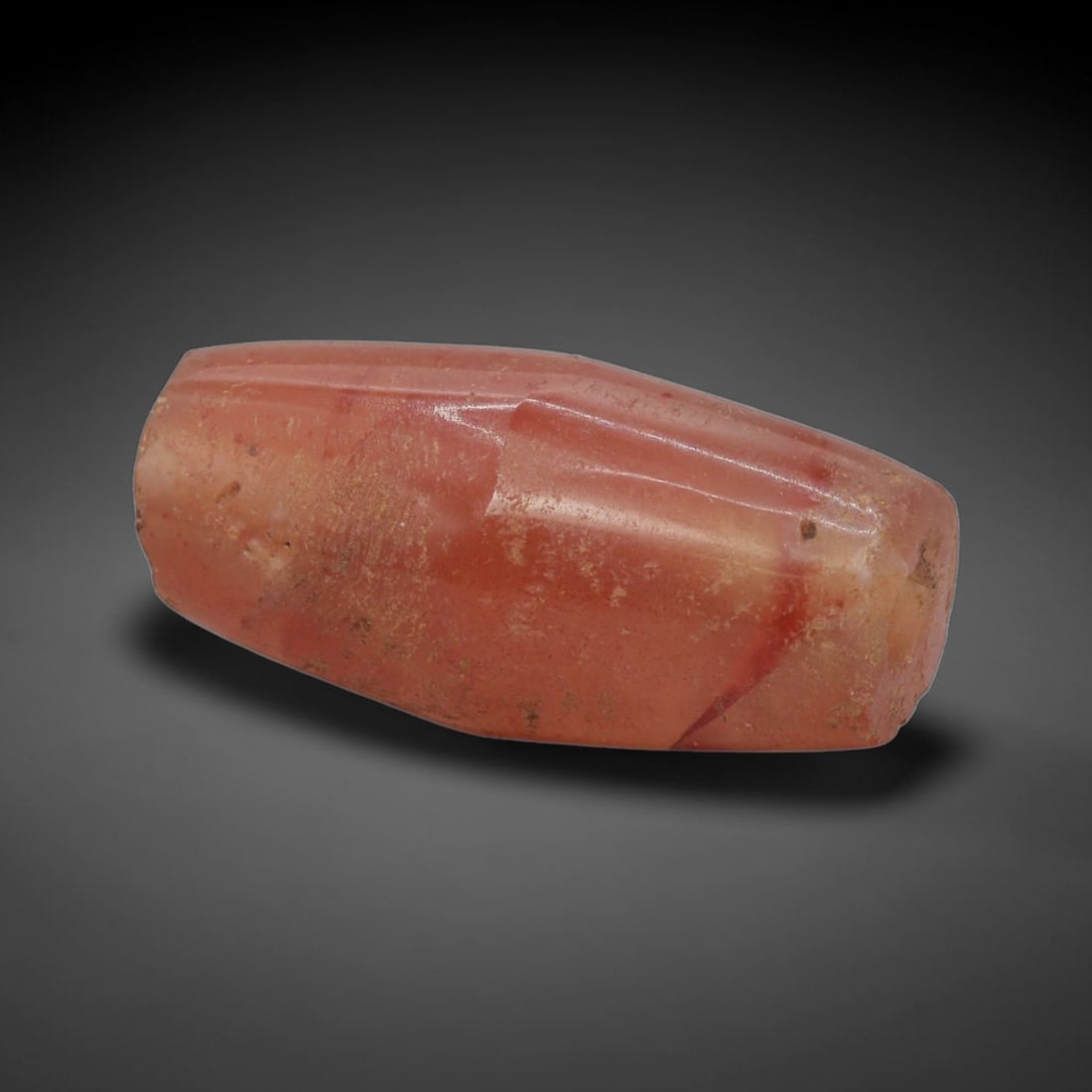 Ancient Agate Bead - Bactrian Faceted Bead, 33XW: This bead is carved from rich carnelian-red agate with subtle creamy-white veining, shaped into a refined faceted barrel form with a precisely centered axial drill hole, characteristic of ancient Bact