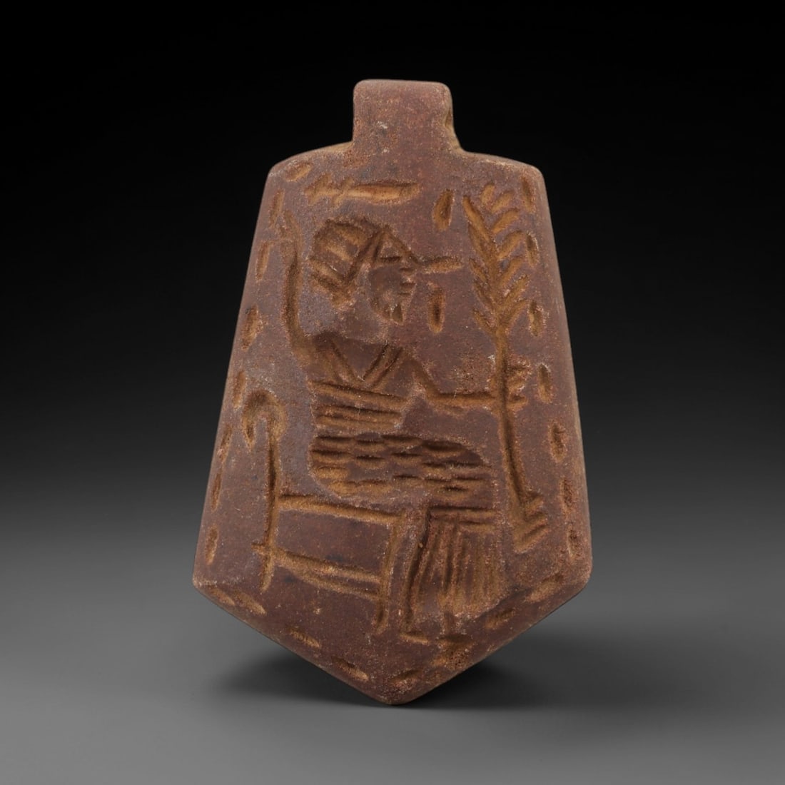 Ancient Steatite Amulet Pendant - Egyptian Figurine, 98AG: Carved from steatite, this ancient Egyptian amulet pendant features a stylized human figure seated with raised arms, set against a background of raised linear and vegetal motifs typical of Egyptian ar