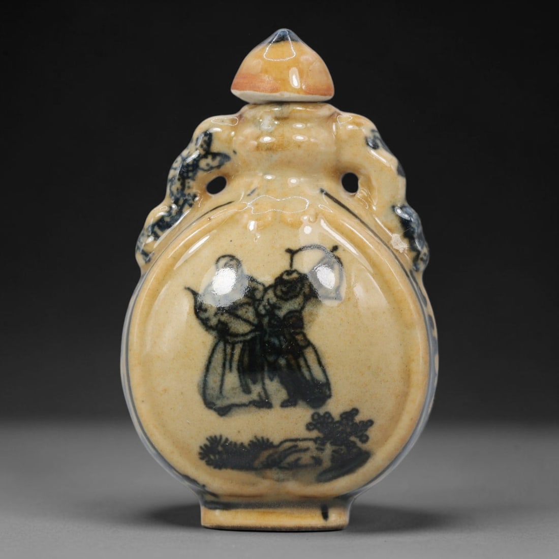 A Chinese Porcelain Moon Flask Snuff Bottle, 20th Century, 60BE: Crafted from porcelain with a pale cream glaze and decorated in underglaze blue, the snuff bottle is formed in a flattened moon flask (bianhu) shape, with molded beast-head handles to either side, a s