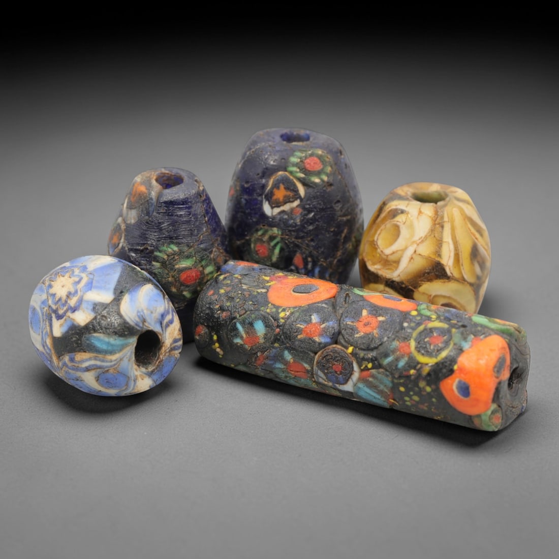 A Group of Venetian Mosaic and Millefiori Glass Beads, 19th-20th Century, 95ZM: Fabricated from opaque and translucent glass, the group consists of six beads of varied forms, including spherical, conical, and cylindrical, each with a central perforation for suspension. One bead d