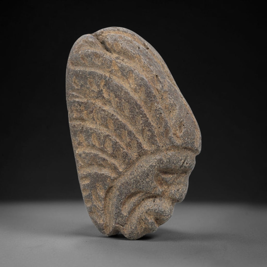 Ancient Stone Maskette - Medieval Human Face Figurine, 52BH: A carved stone maskette of irregular form, fashioned from a single piece of weathered grey stone with natural mineral staining. The front is carved in deep relief to depict a stylized human face in pr
