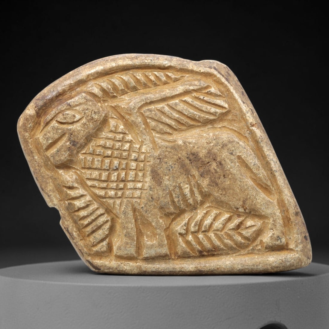 Ancient Stone Plaque Relief - Near Eastern Winged Ibex Figurine, 11ZY: Carved from a single piece of stone, this irregularly shaped relief plaque depicts a stylized winged ibex, rendered in the linear, incised artistic tradition of the ancient Near East. The figure is de