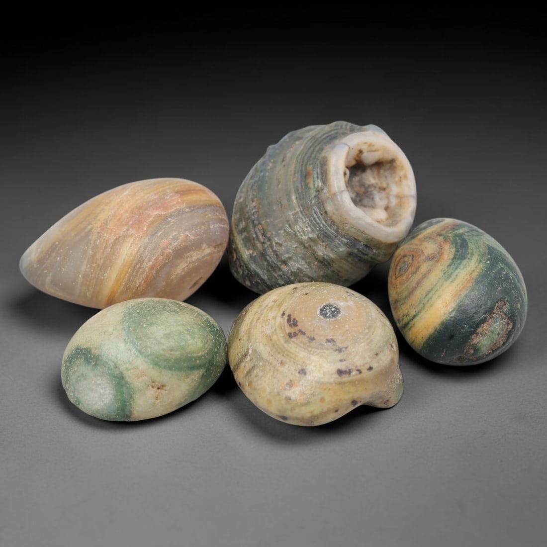 A Group of Five Mongolian Agate Eye Beads, 49BH: The group comprises five banded agate beads, each shaped to highlight the stone's natural concentric "eye" formations. The beads vary in form: three are ovoid, one is teardrop-shaped, and one is barre