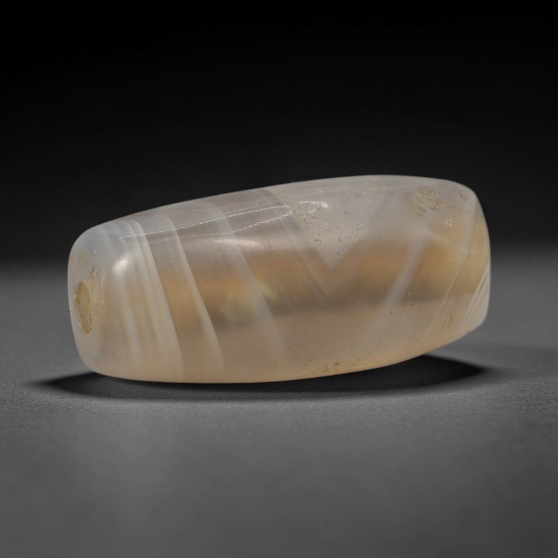 Ancient Agate Bead - Bactrian Banded Barrel Bead, 30XW: This bead is carved from translucent milky-grey banded agate, shaped into a smooth, elongated barrel form with a precisely centered axial drill hole, characteristic of ancient Bactrian lapidary crafts