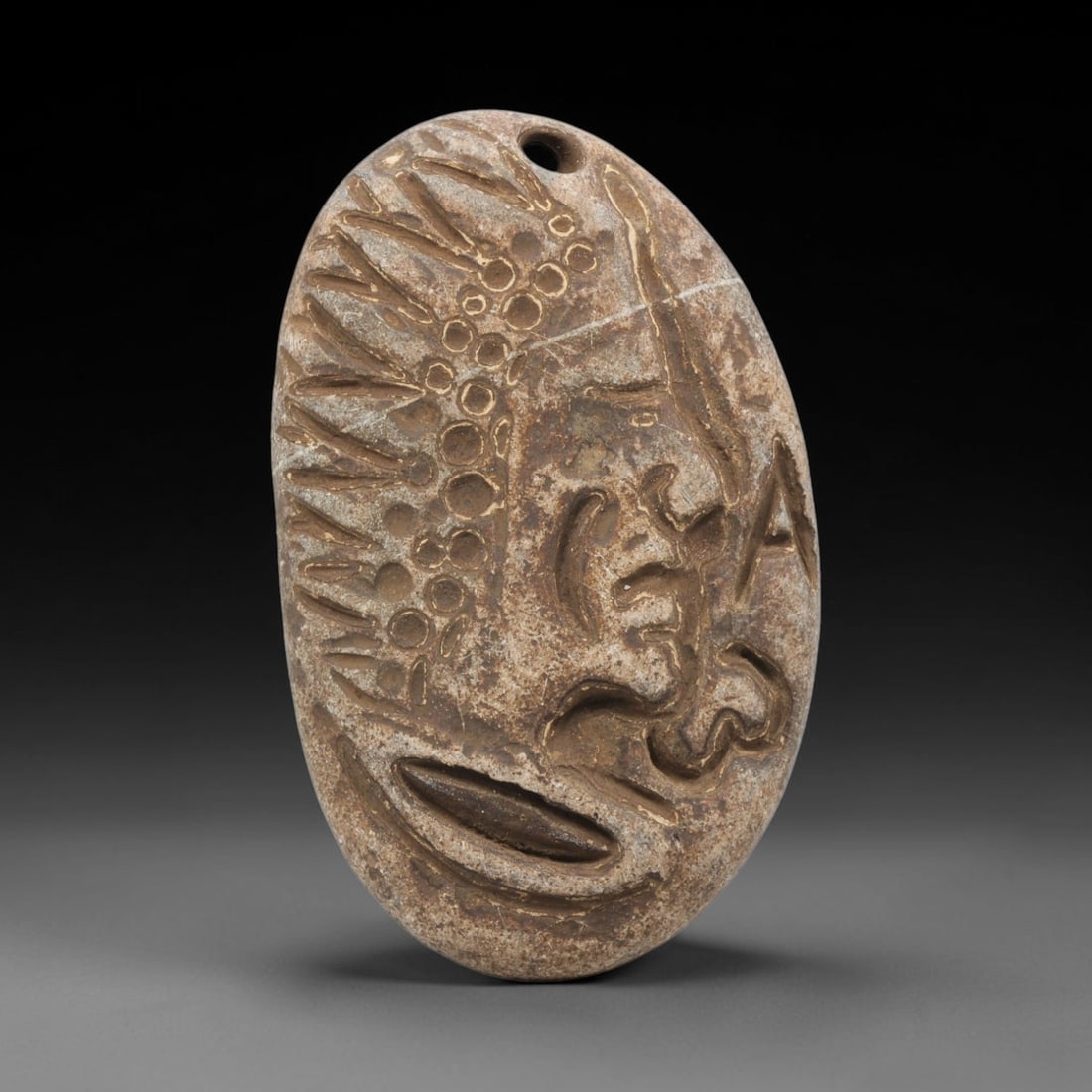 Ancient Stone Amulet - Medieval Human Face Pendant, 44BH: A carved stone amulet of oval form, fashioned from a single piece of weathered stone with natural mineral staining and a visible hairline crack. The front is carved in deep relief to depict a stylized