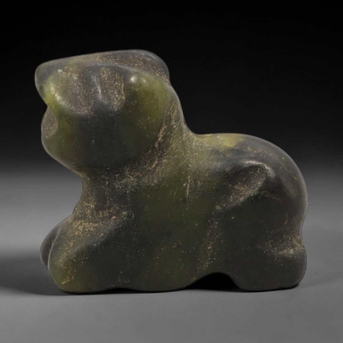 Ancient Stone Animal Amulet - Near Eastern Zoomorphic Figurine, 4XR: This amulet is carved from a mottled green stone, shaped into a stylized crouching animal form with a perforated suspension hole at the upper back, confirming its use as a wearable protective charm. T