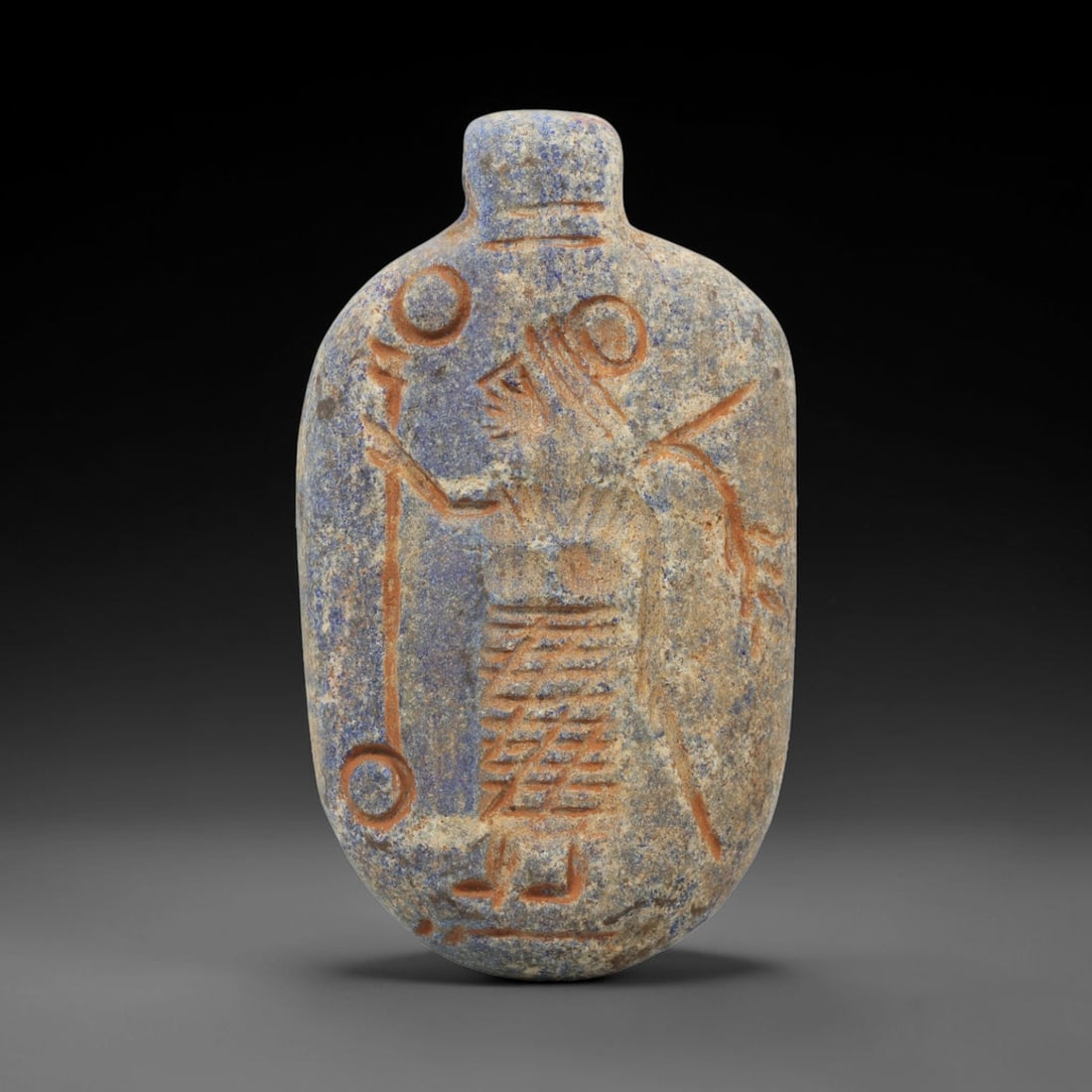 Ancient Lapis Lazuli Amulet - Near Eastern Deity Figure, 38ZX: Carved from lapis lazuli, this amulet features a relief depiction of a standing deity or ritual figure, rendered in the stylized glyptic tradition of the ancient Near East. The figure is detailed with