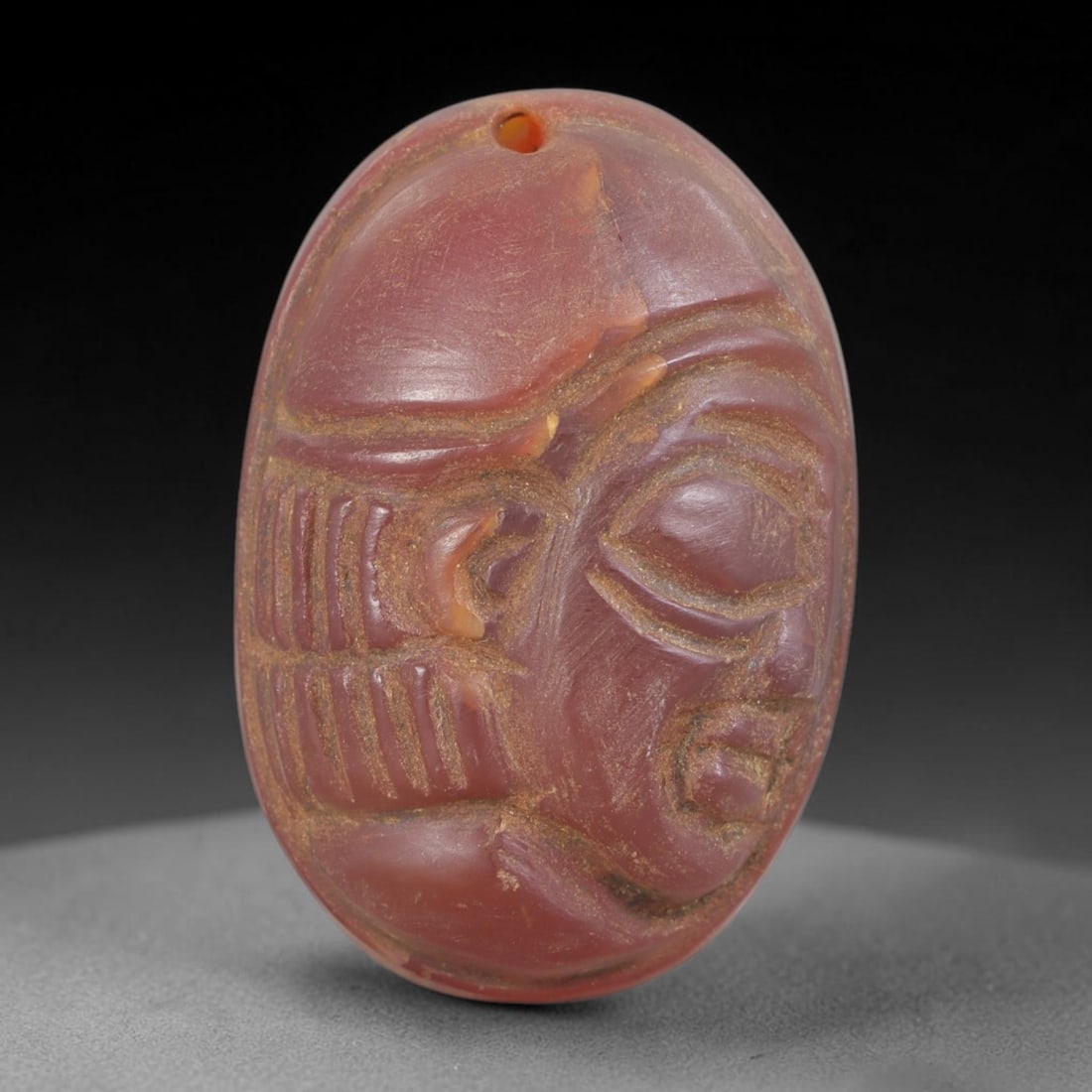 Ancient Carnelian Head Plaque - Near Eastern Amulet, 49FY: Carved from a rich reddish-brown carnelian, this amulet takes the form of a stylized human head in high relief, set within an oval plaque, characteristic of ancient Near Eastern amuletic and glyptic t