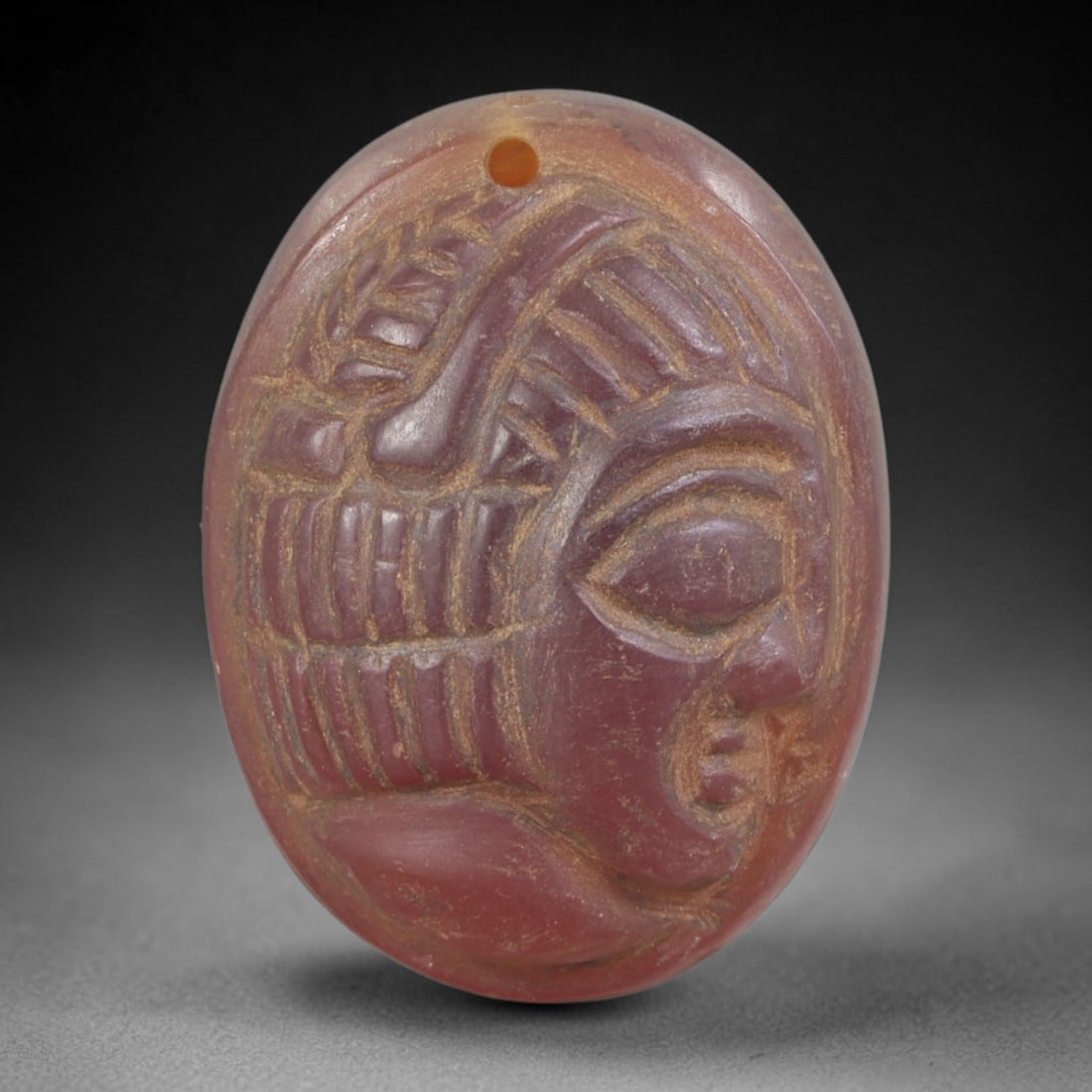 Ancient Carnelian Head Plaque - Near Eastern Amulet, 50FY: Carved from a rich reddish-brown carnelian agate, this amulet takes the form of a stylized human head in high relief, set within an oval plaque, reflecting the glyptic and amuletic traditions of ancie
