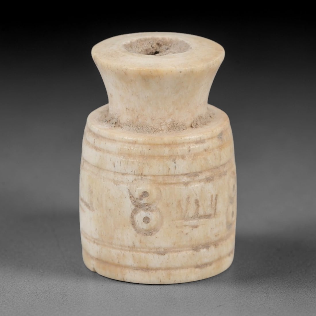 Ancient Bone Spindle Whorl - Near Eastern Dot-in-Circle Motif, 86XR: This ancient Near Eastern spindle whorl is crafted from bone, featuring incised geometric decoration with a prominent dot-in-circle motif encircling the central aperture. The form is a compact, cylind