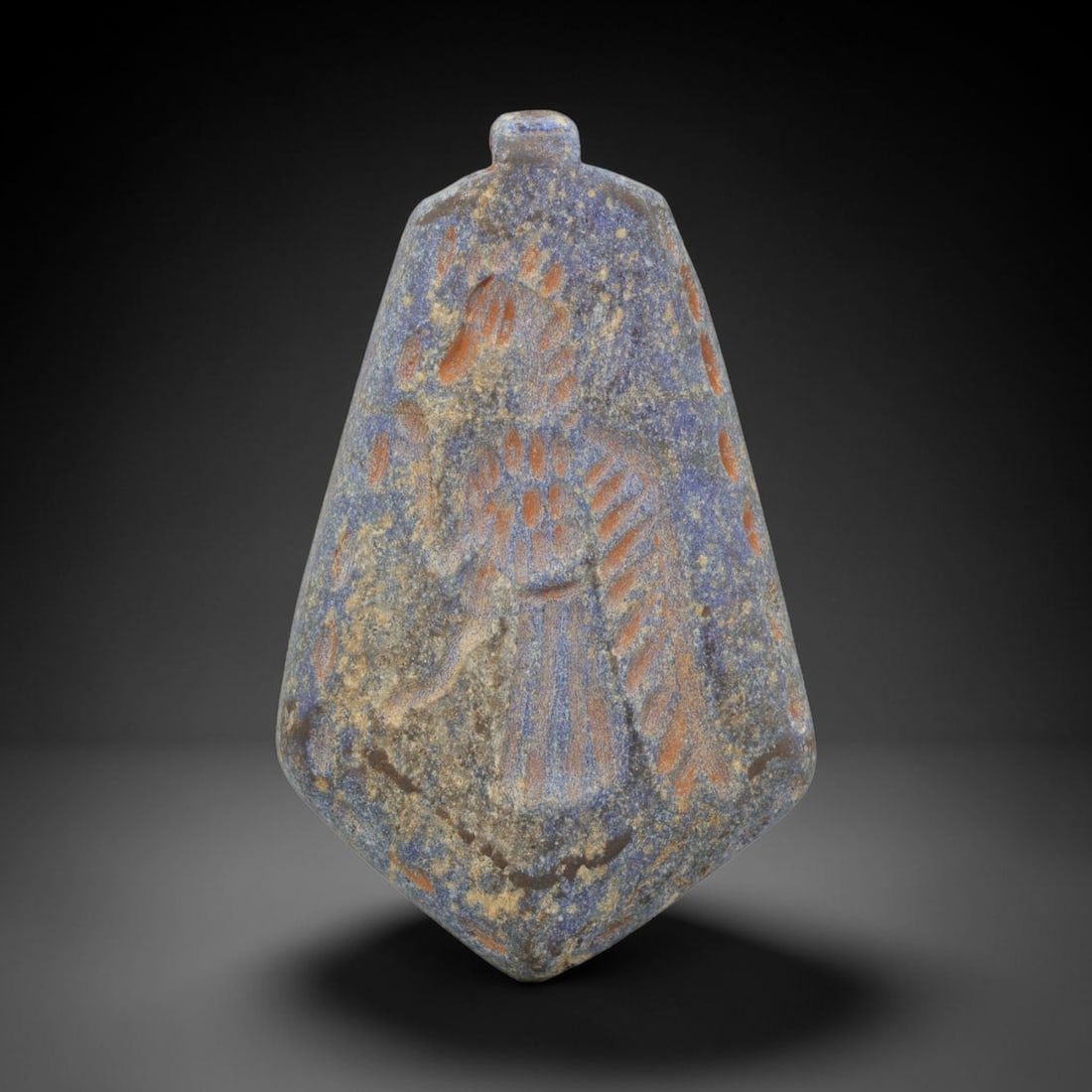 Ancient Lapis Lazuli Amulet - Near Eastern Winged Figure, 5ZX: Carved from lapis lazuli, this amulet features a relief depiction of a standing winged humanoid figure, rendered in the stylized glyptic tradition of the ancient Near East. Incised details define the