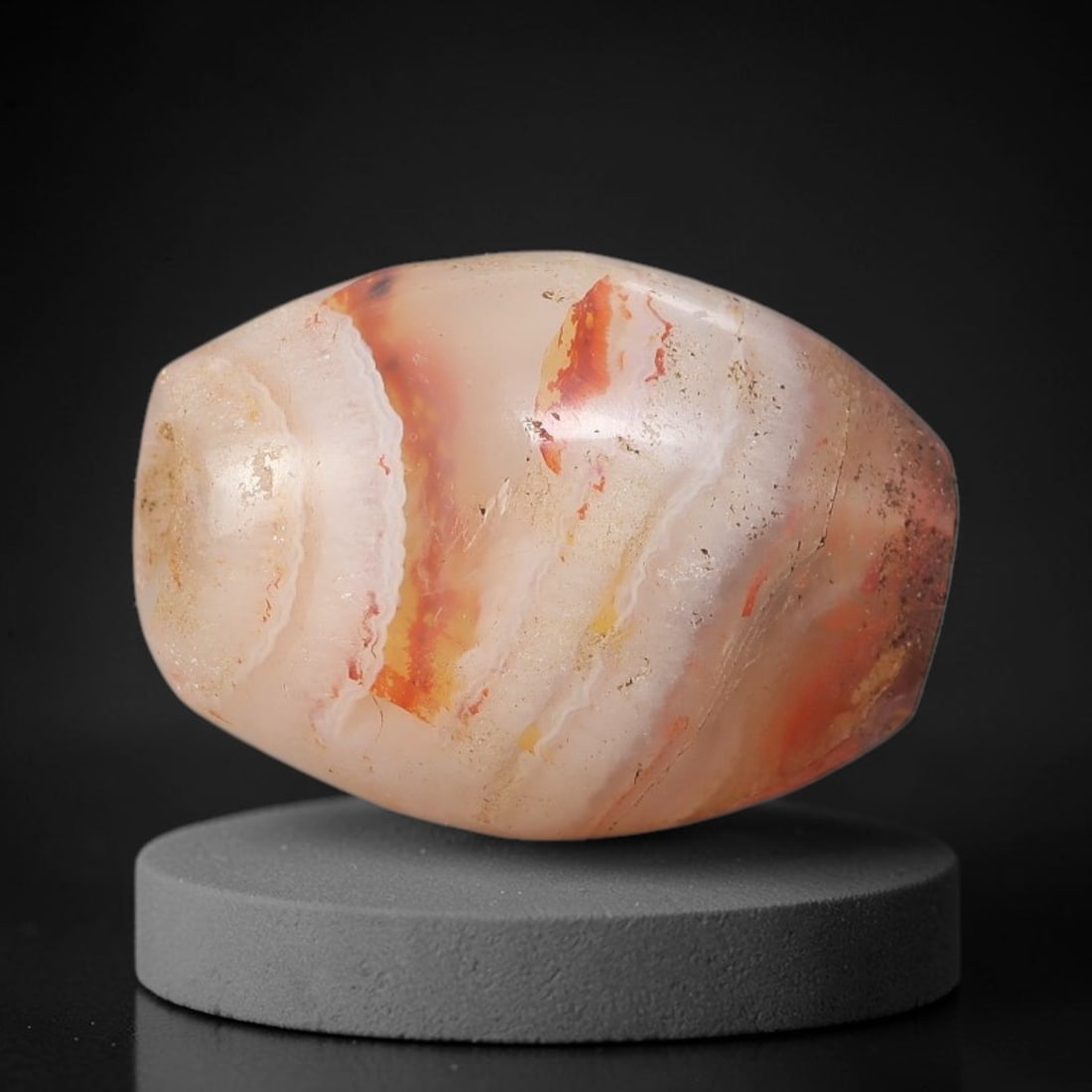 Ancient Banded Agate Bead - Near Eastern Artifact, 98BC: This artifact is crafted from natural banded agate, shaped into a rounded barrel form with striking concentric banding in warm cream, fiery orange-red, and soft peach hues. The bead features a central